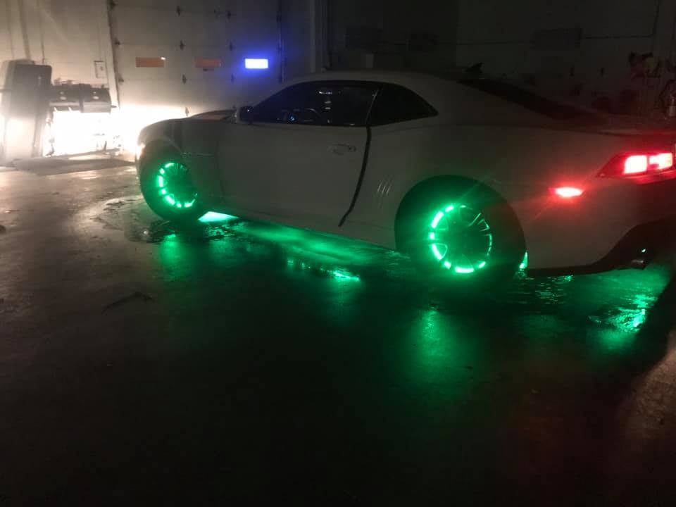 White car with green LED underglow and wheel lights, parked at night.