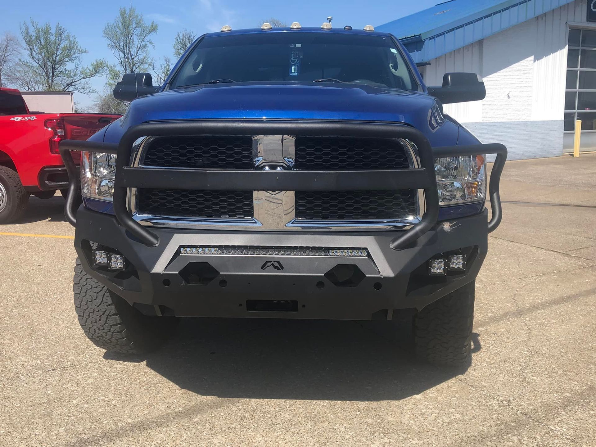 Blue Dodge Ram truck with custom bumper and light bar, parked outdoors.