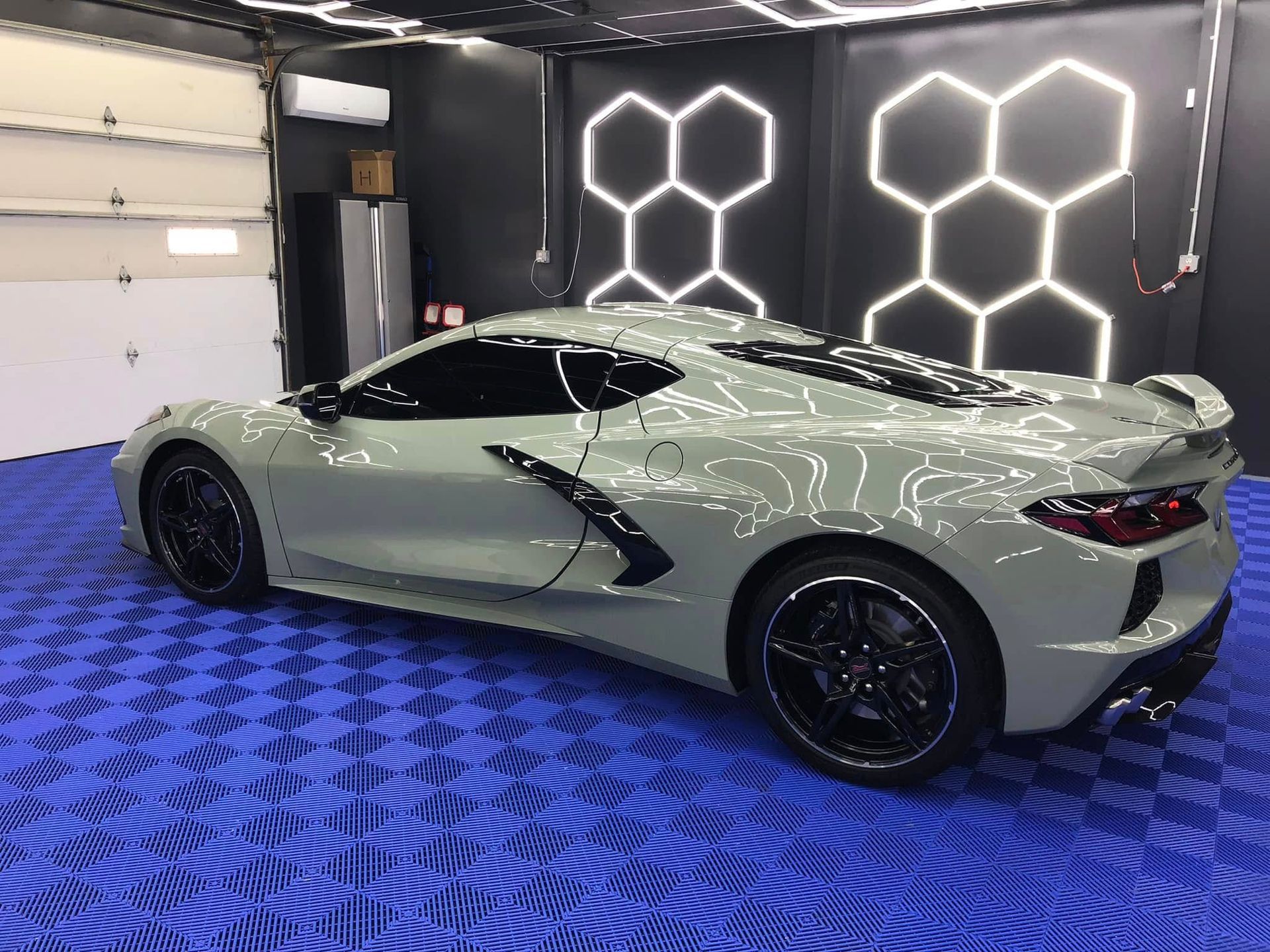Gray sports car inside a car detailing shop. Black wheels, tinted windows. Blue tiled floor.