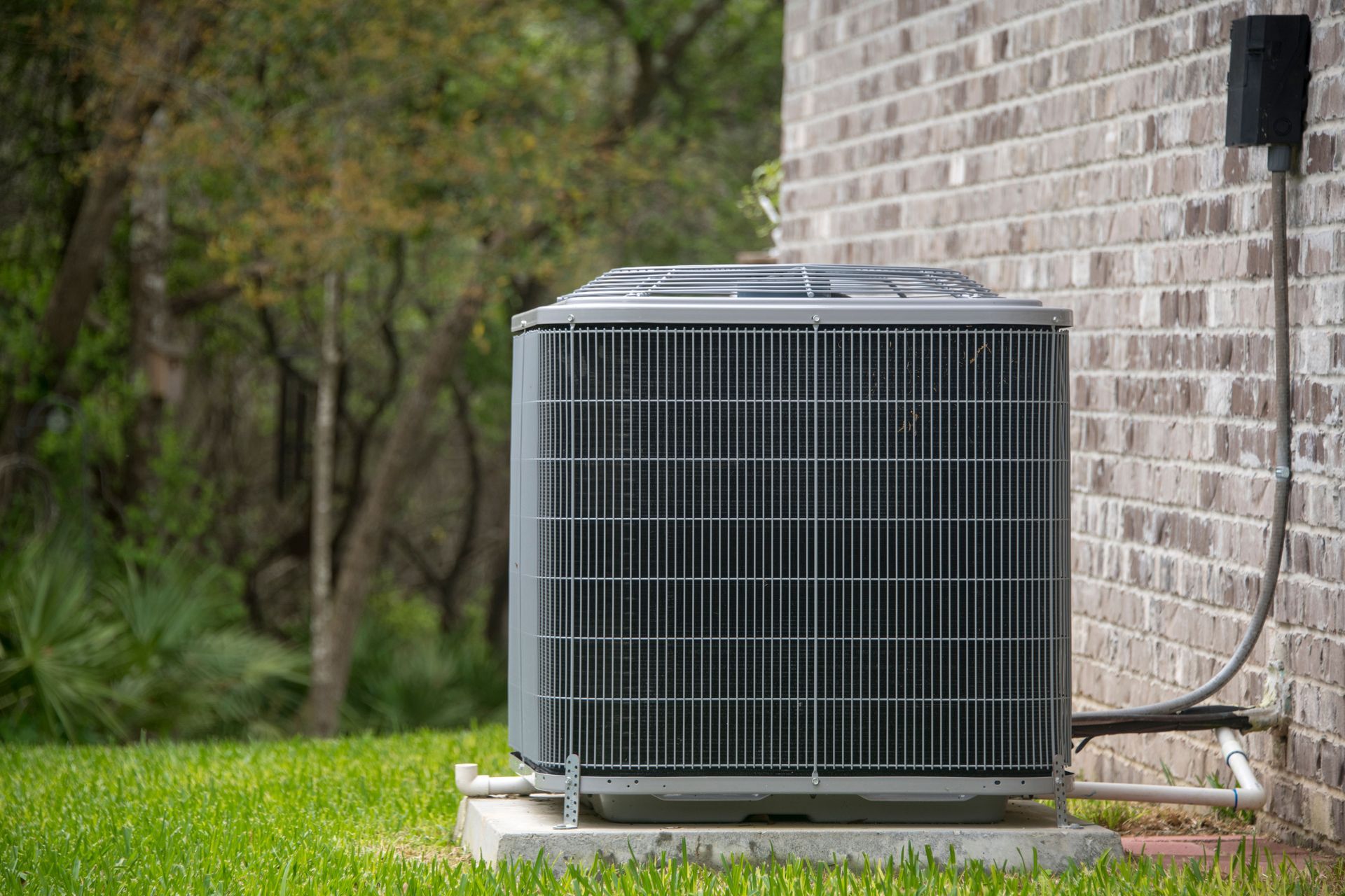 Outdoor air conditioner unit beside a brick house on a grassy lawn