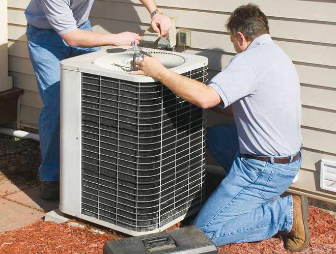 Two technicians servicing a home air conditioner unit outside a house