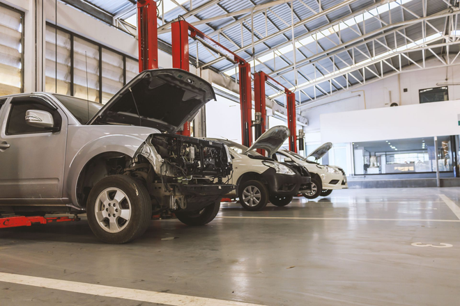 Cars in an auto repair shop, with one silver SUV hood open on a lift bay.