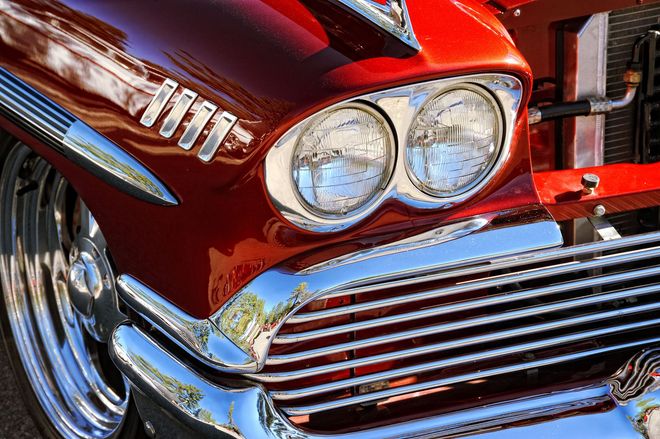 Close-up of a shiny red vintage car front with chrome grille and dual round headlights