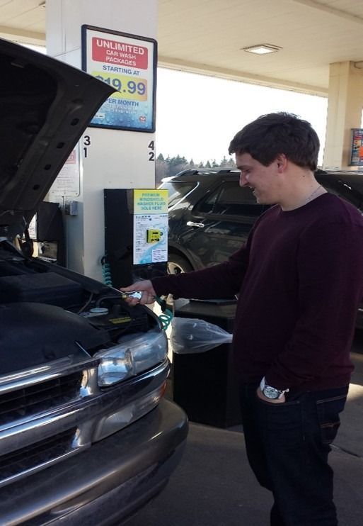 A man looking under the hood of a car at a gas station