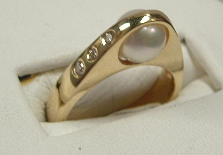 Gold ring with a pearl and four small diamonds, set on a white surface.