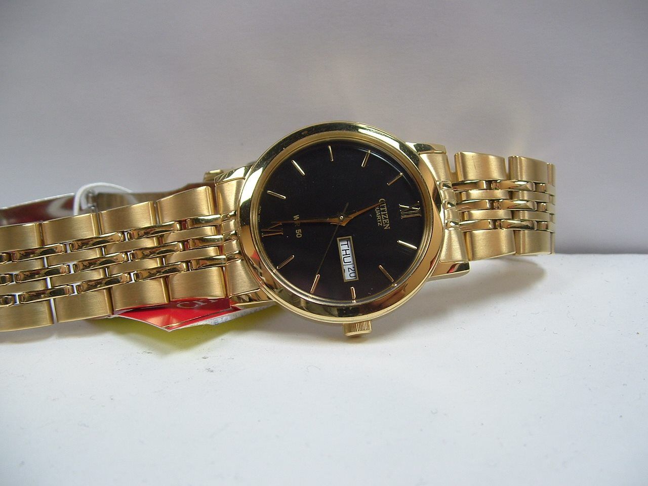 Gold wristwatch with a black face and date display, lying on a white surface.