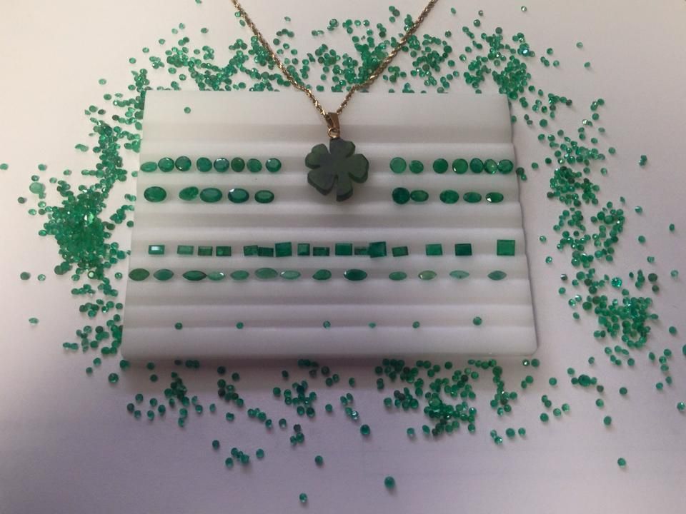 Emerald gemstones and clover pendant on a white surface. Green gems scattered around.