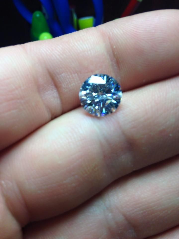 A light blue, round gemstone rests in the palm of a hand. Other items are blurred in the background.