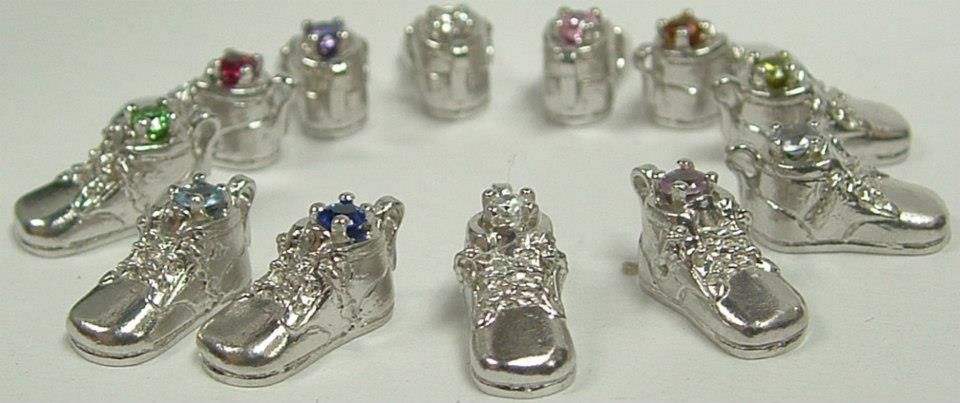 Silver sneaker charms and small, round charms with different-colored stones arranged in a circle on a white surface.