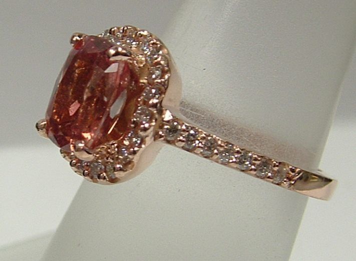 Rose gold ring with a rectangular, orange-pink center stone, haloed by smaller diamonds; diamonds also line the band.