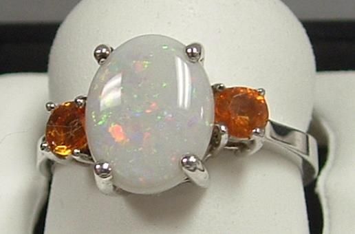 Oval white opal ring with two orange gemstone side stones, set in silver.