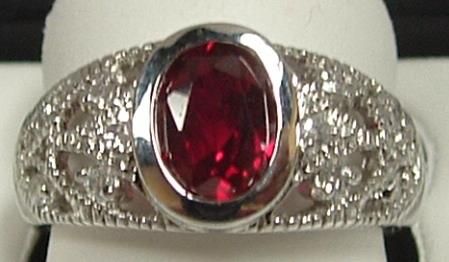 Silver ring with a bezel-set, oval, red gemstone and a decorative, floral-patterned band.