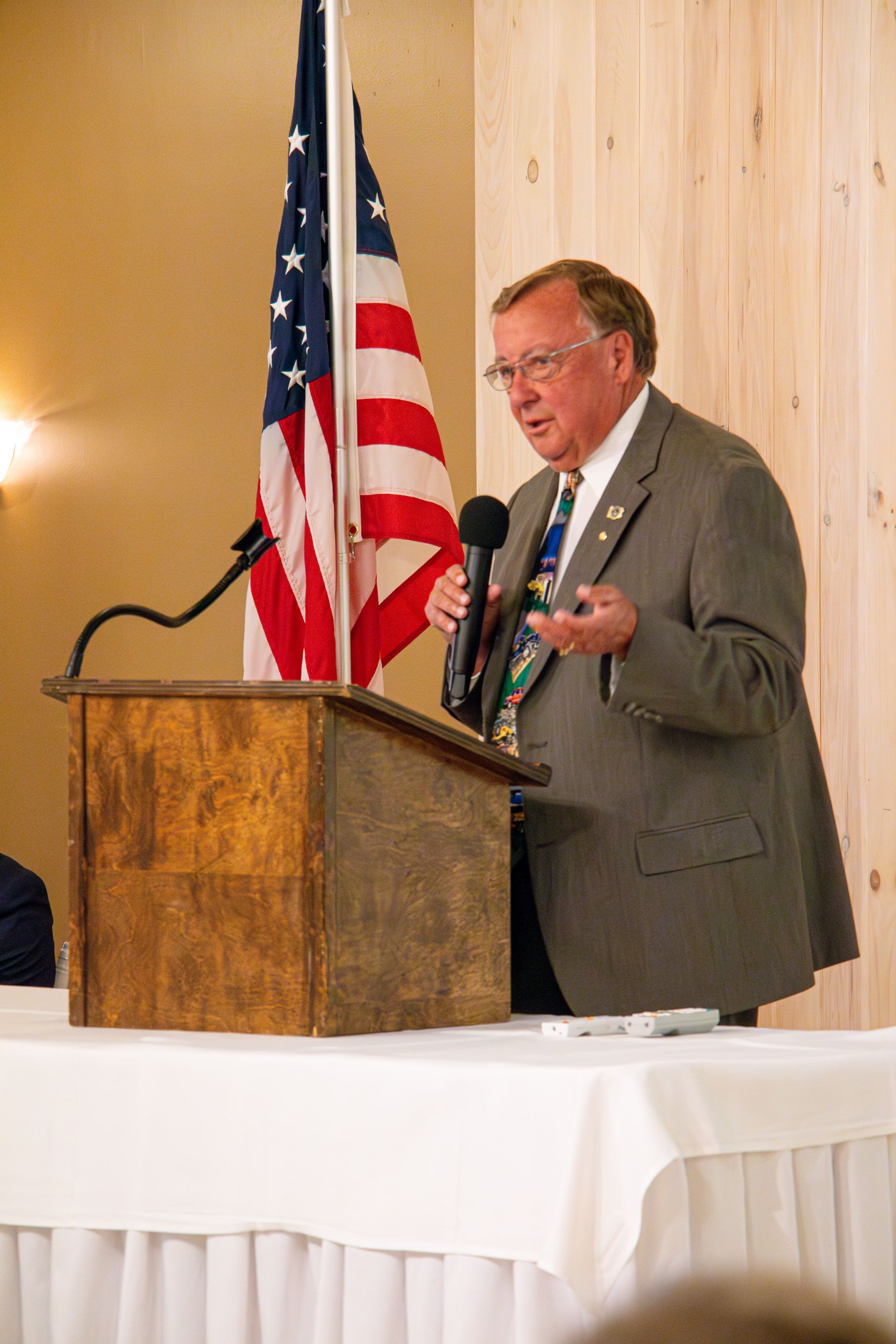 A man in a suit and tie is giving a speech at a podium in front of an american flag.
