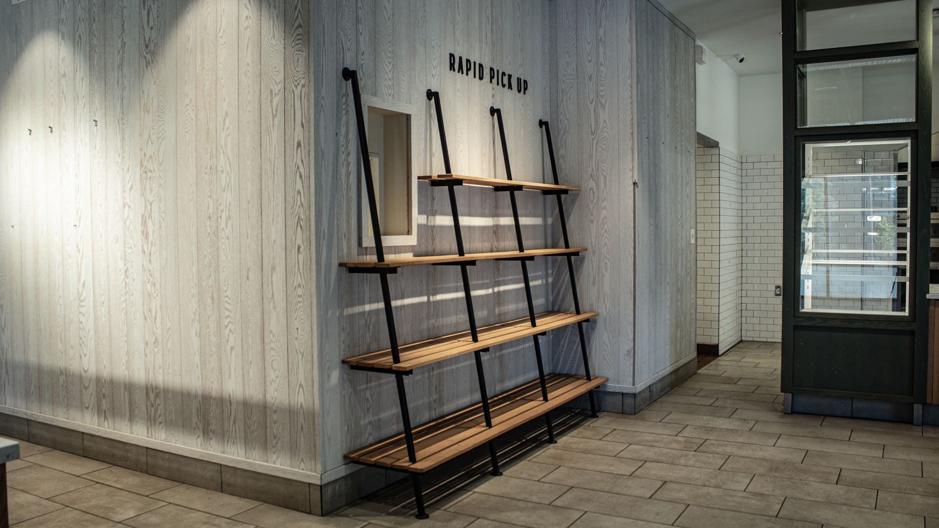 Empty storefront interior with black metal shelving against a white wall and a glass door.