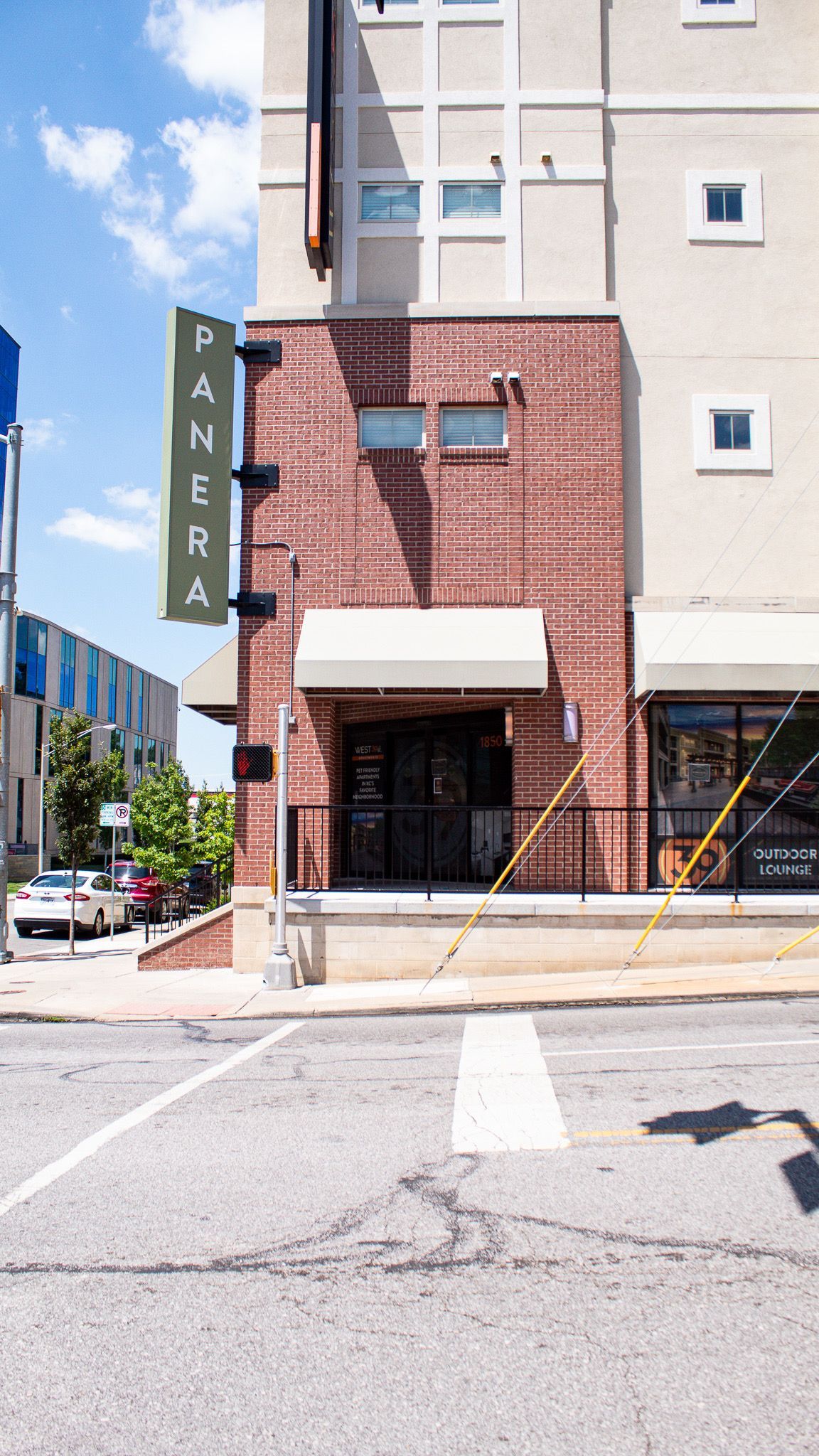 Brick building entrance with green vertical sign on a sunny street corner
