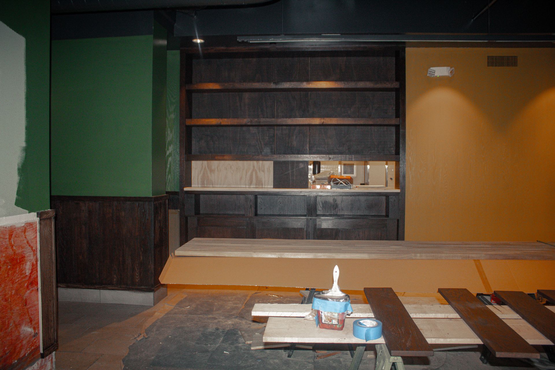 Empty restaurant seating area with low tables, benches, and a lit shelf against dark wood walls