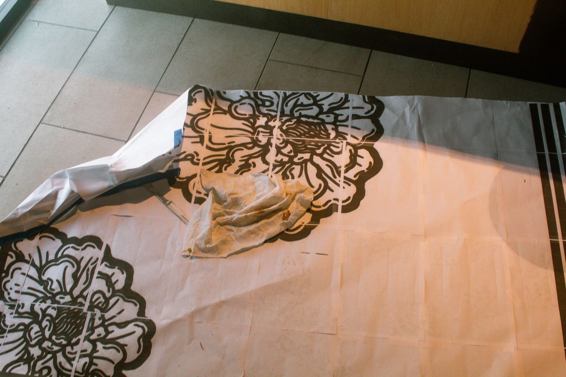Crumpled floral tablecloth with a torn corner on a tiled floor near a wall.