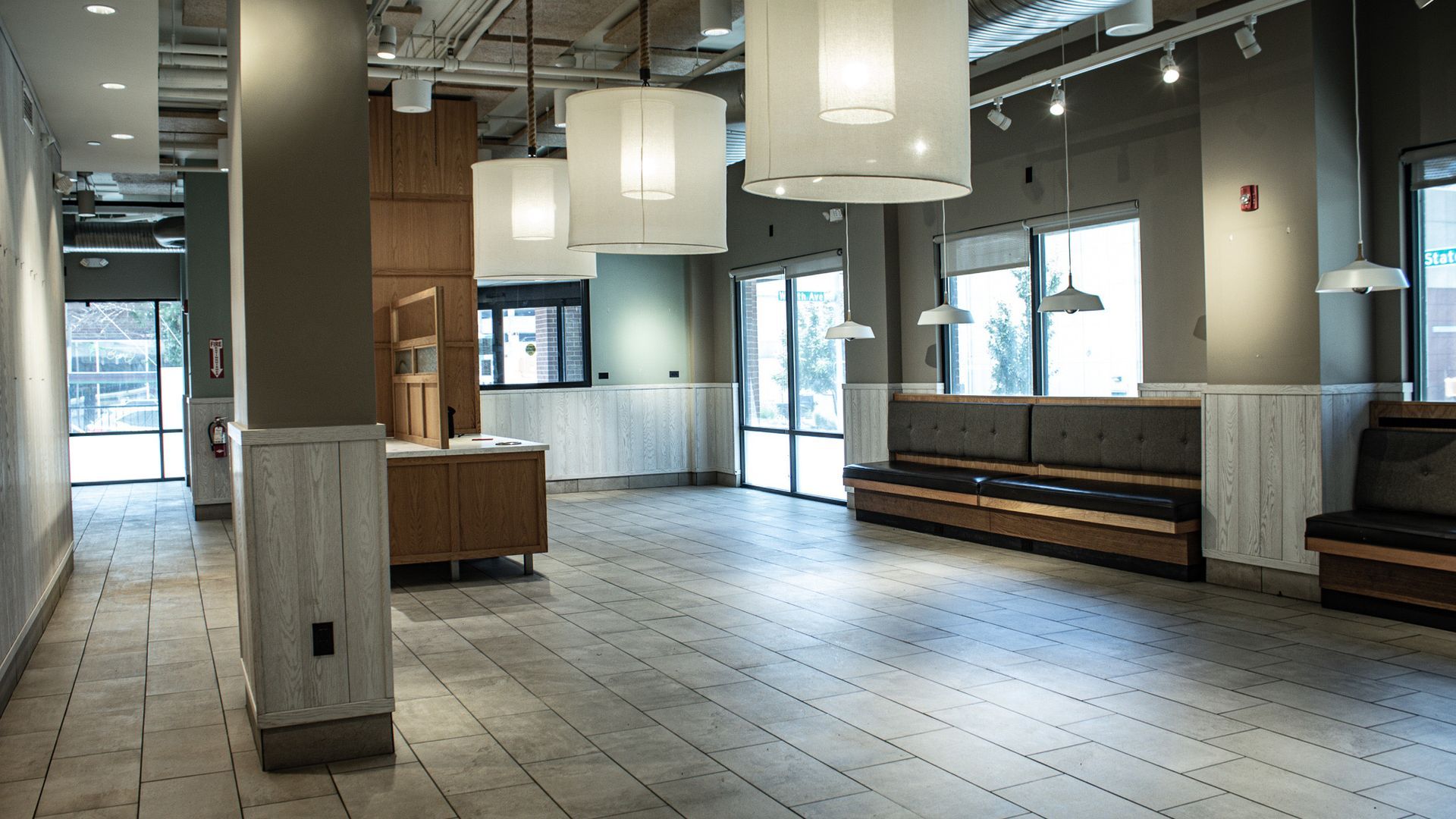 Empty modern lobby with tiled floor, hanging lights, benches, and large windows near the entrance