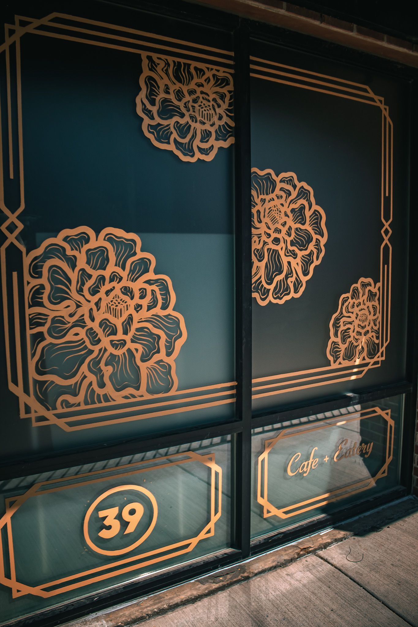 Teal storefront window with gold floral designs and the number 39 on the lower panel.