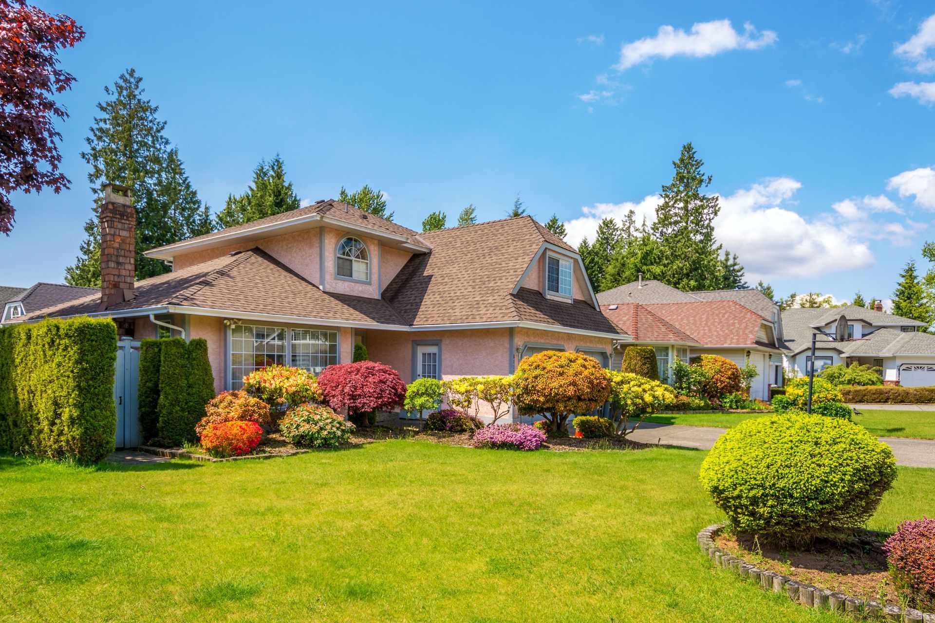Suburban house with a manicured lawn, colorful shrubs, and blue sky on a sunny day