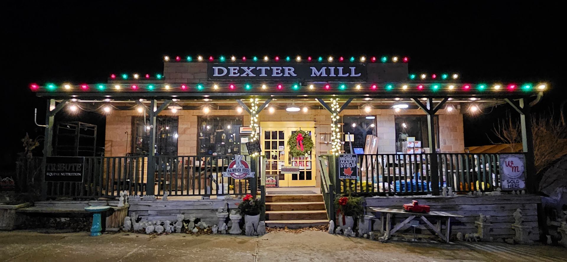 Night-lit storefront with colorful string lights, steps, benches, and “Bistro Mill” sign at the entrance