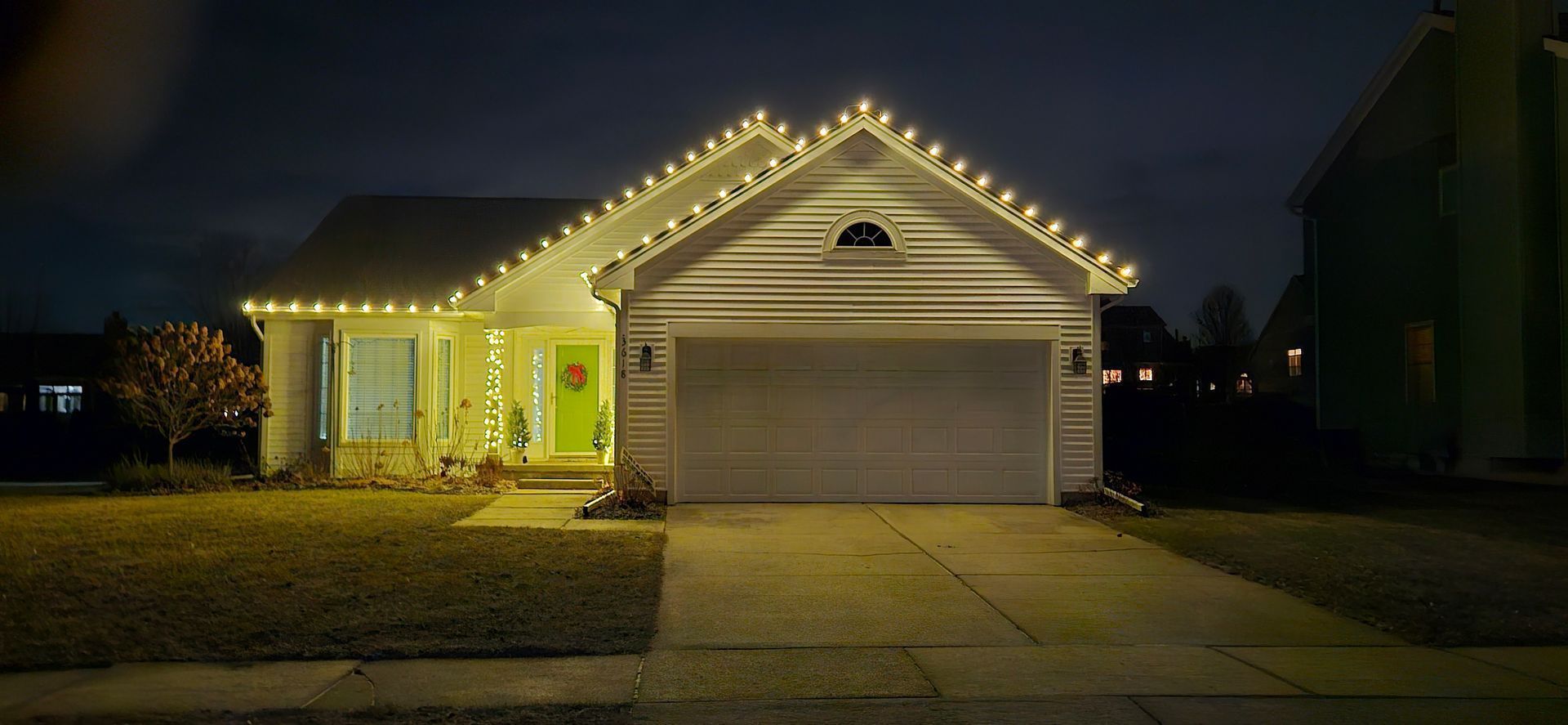 Suburban house at night outlined with warm white Christmas lights, garage door closed.