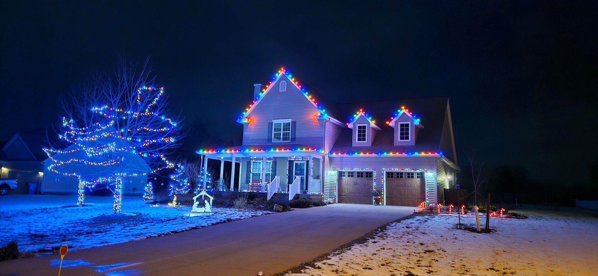 Snowy house decorated with blue and white Christmas lights at night