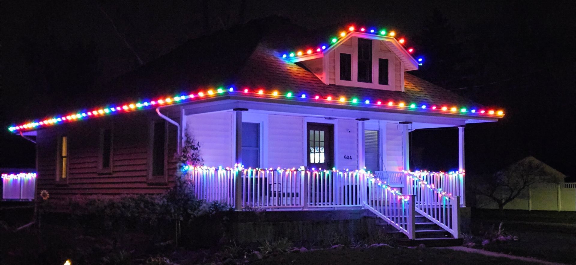 House outlined with colorful Christmas lights at night, with white porch and steps