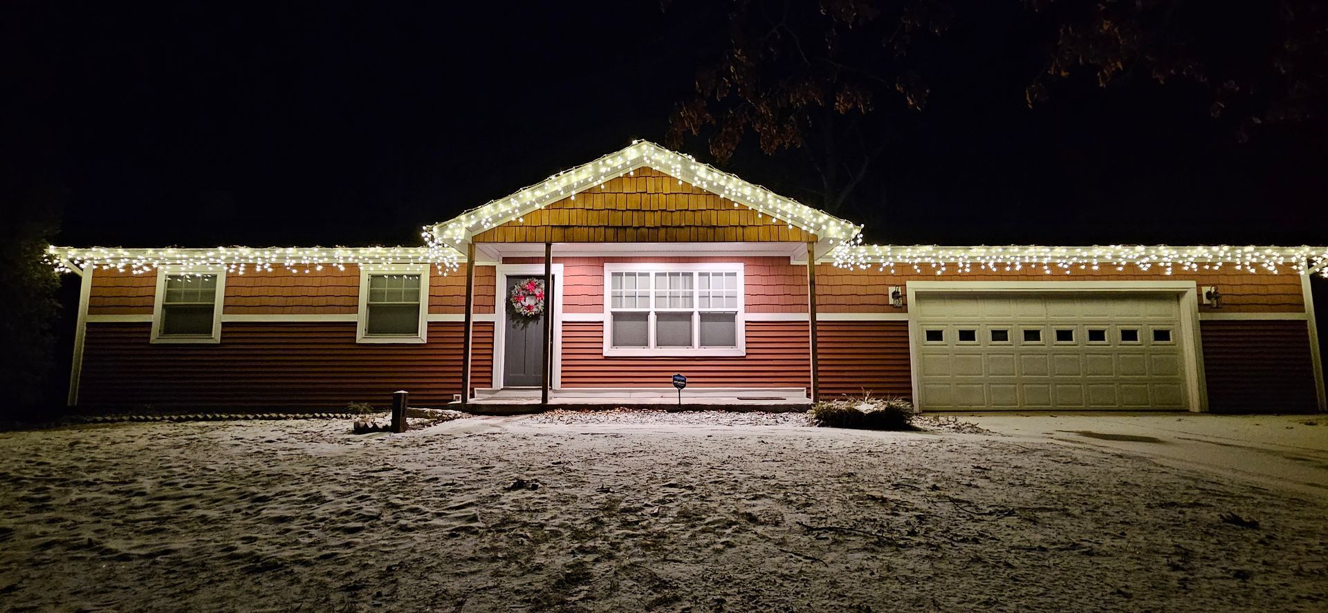 Snow-covered house at night with warm holiday lights along the roof and windows.