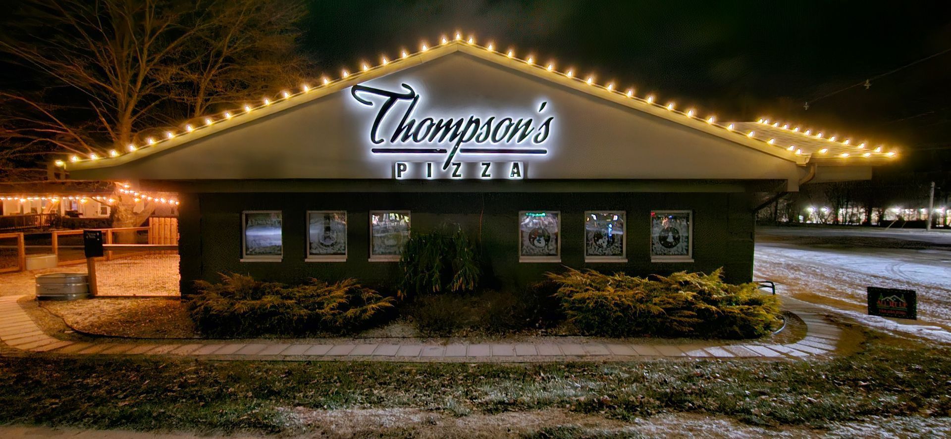 Nighttime view of Thompson's building lit by string lights, with snow on the ground
