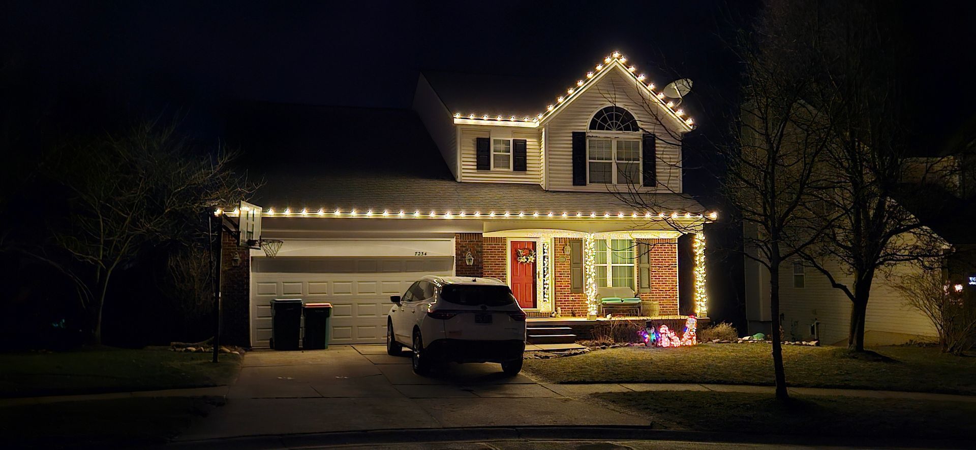 House lit with Christmas lights at night, with a SUV parked in the driveway.