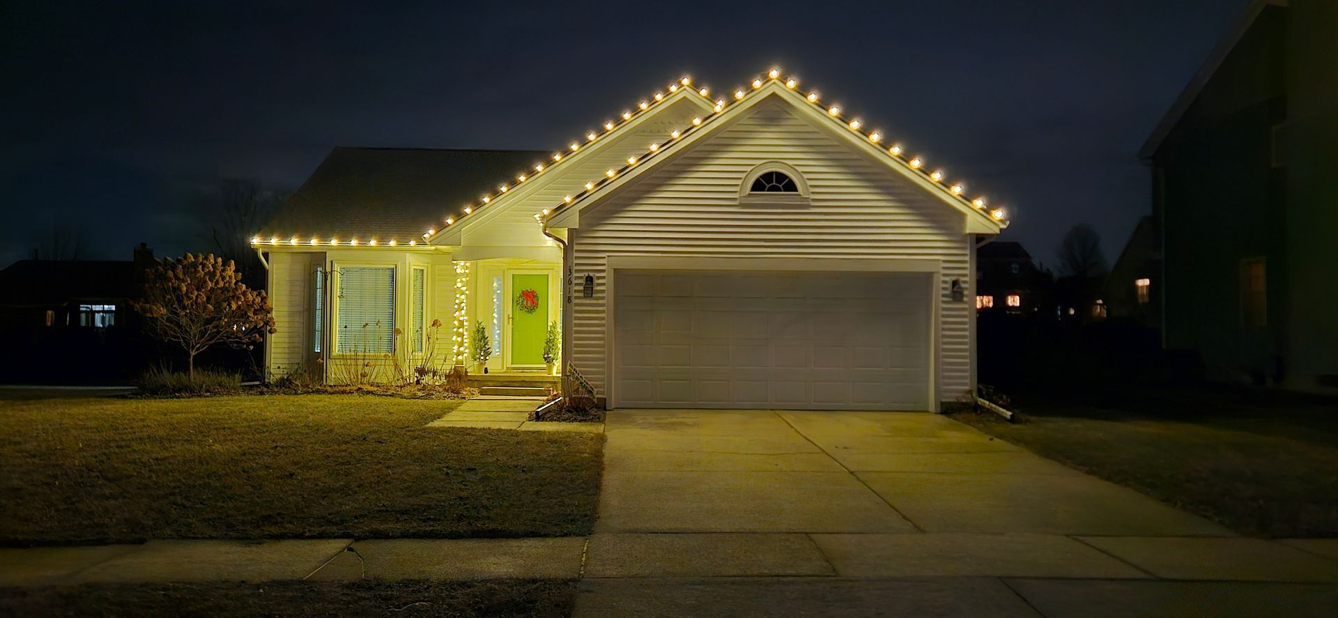 House with Christmas lights glowing at night, garage door closed, lit front porch and driveway