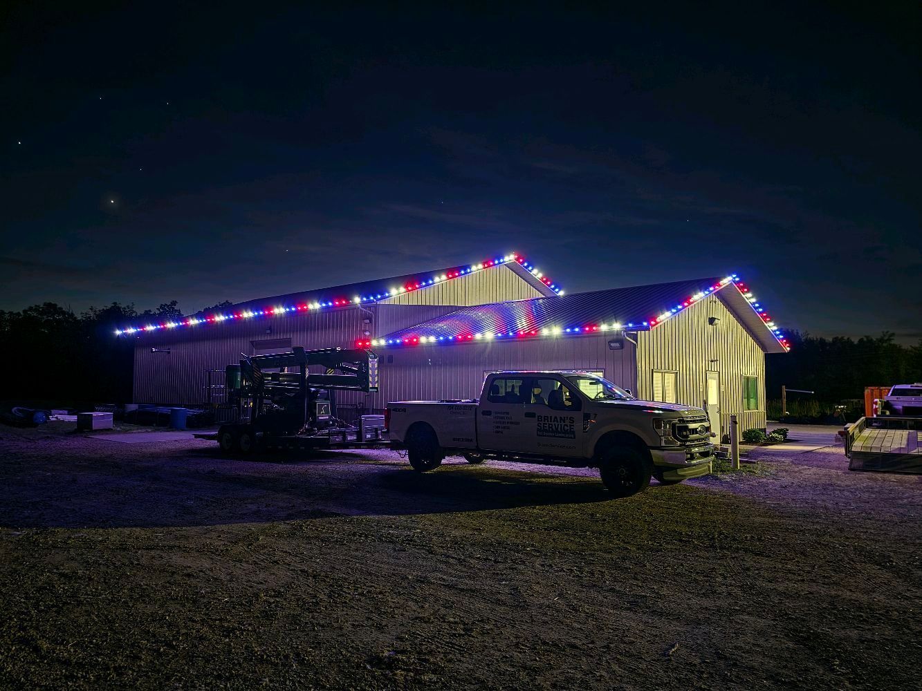 Night scene of a lit event tent and parked trucks on a gravel lot