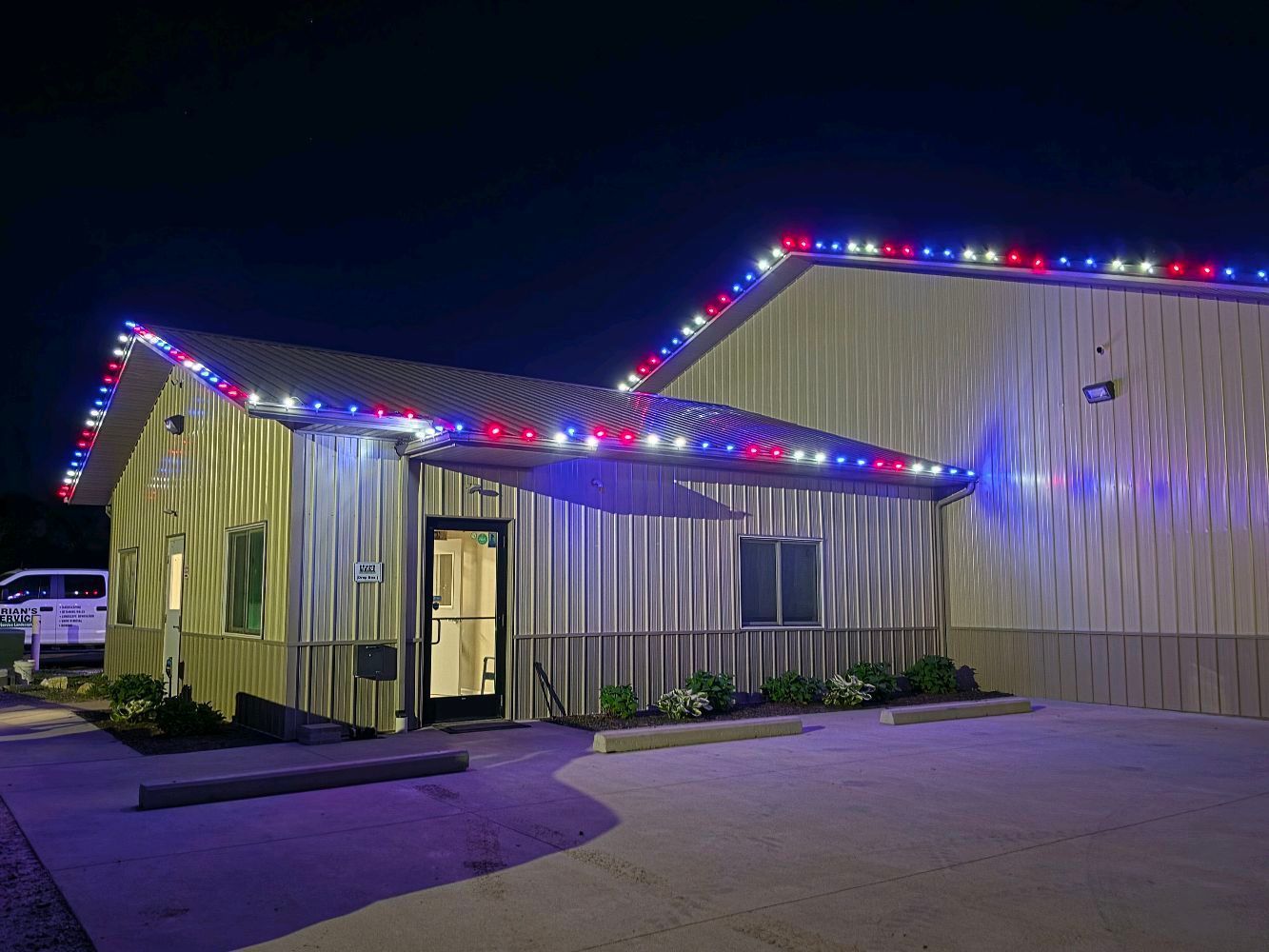 Industrial building at night with red, blue, and white holiday lights along the roofline.