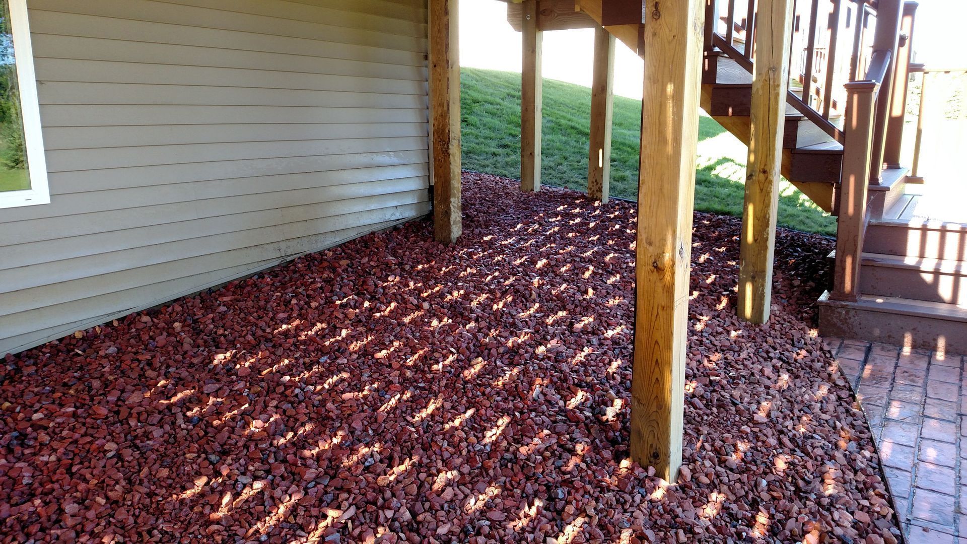 Mulched garden bed beside a house deck with wooden posts and stairs
