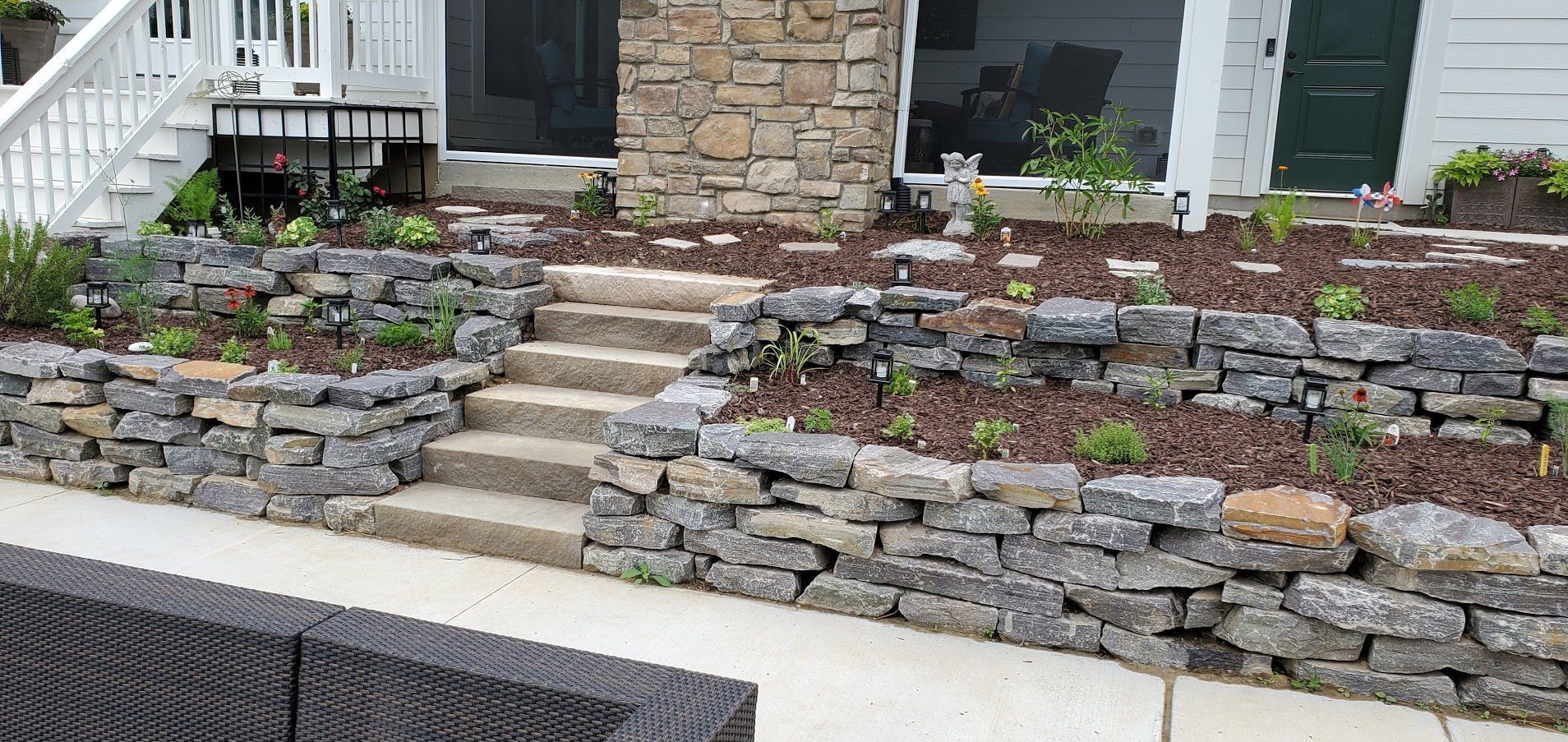 Stone terraced front steps with landscaped retaining walls leading to a house entrance