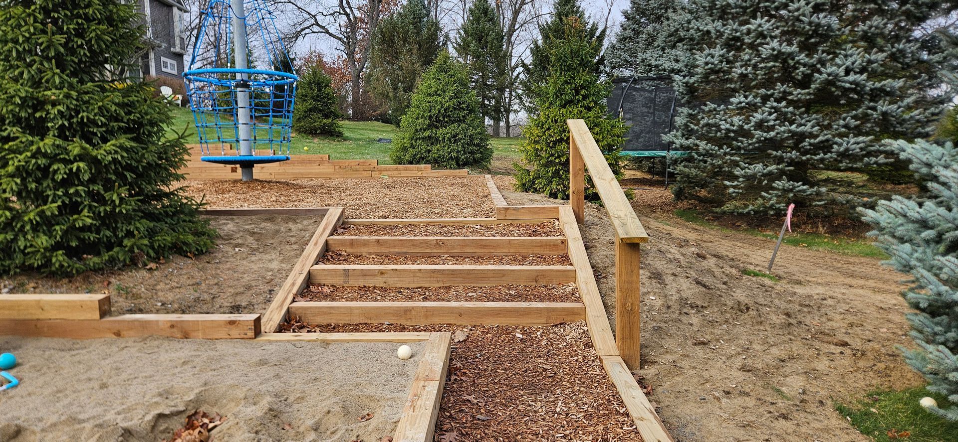 Wooden steps with railings leading up a landscaped garden path lined with trees and shrubs