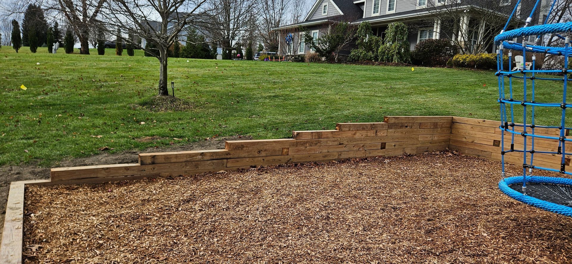 Mulched garden bed with stacked stone border beside a grassy yard and house