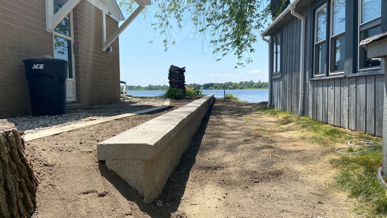 Concrete ramp between buildings leading to a waterfront walkway under a clear blue sky.