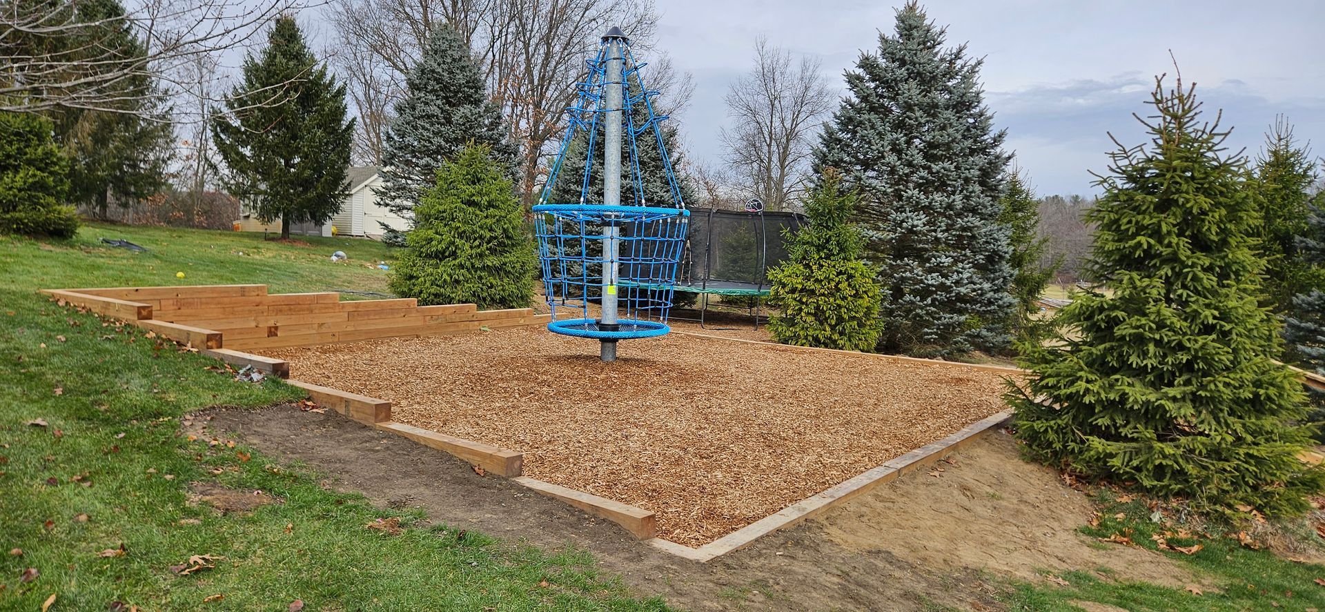 Blue metal sculpture in a mulched park bed surrounded by evergreen trees and grass