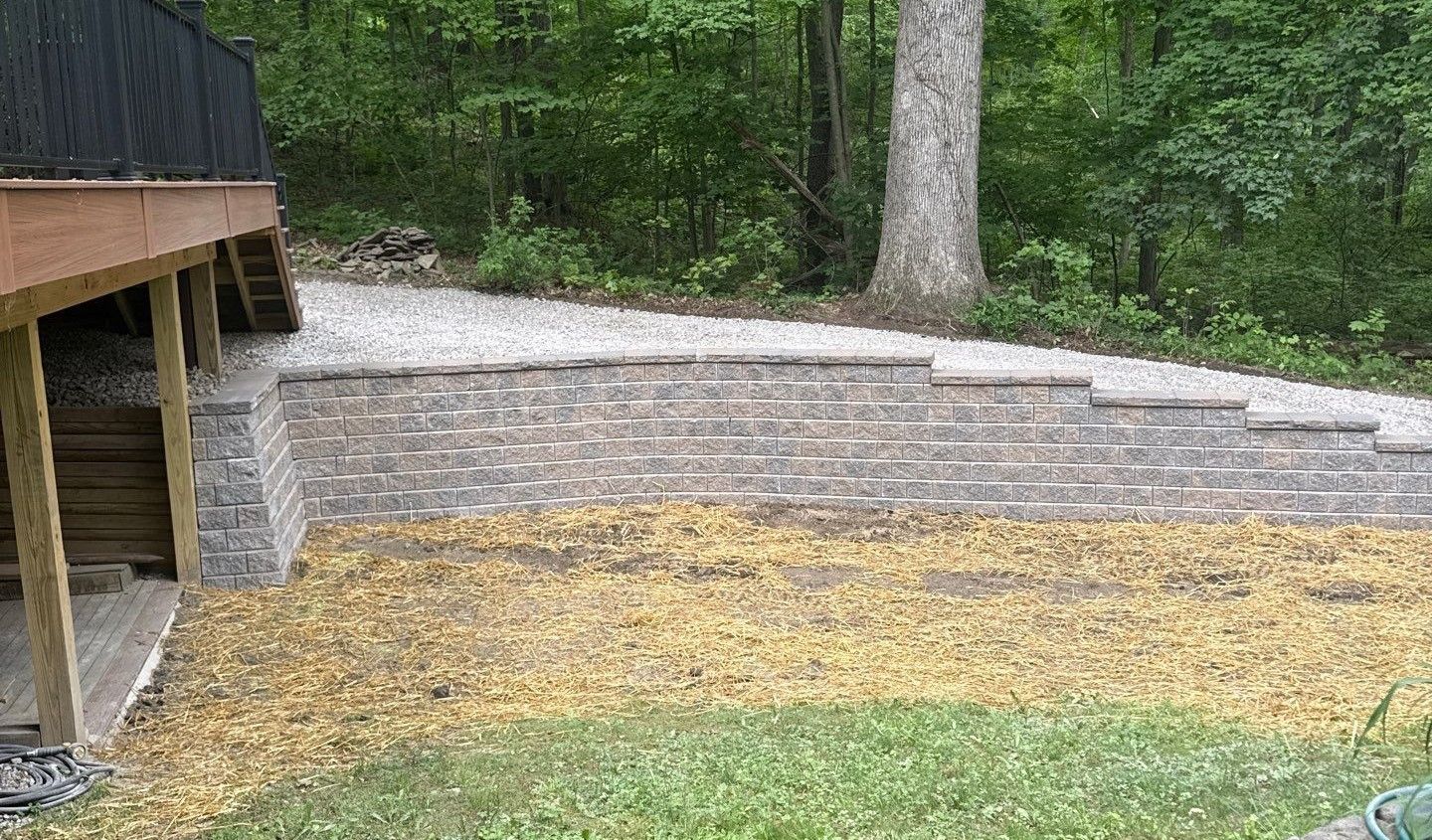Wooden deck overlooking a gravel and stone path in a wooded backyard, with grass and trees nearby