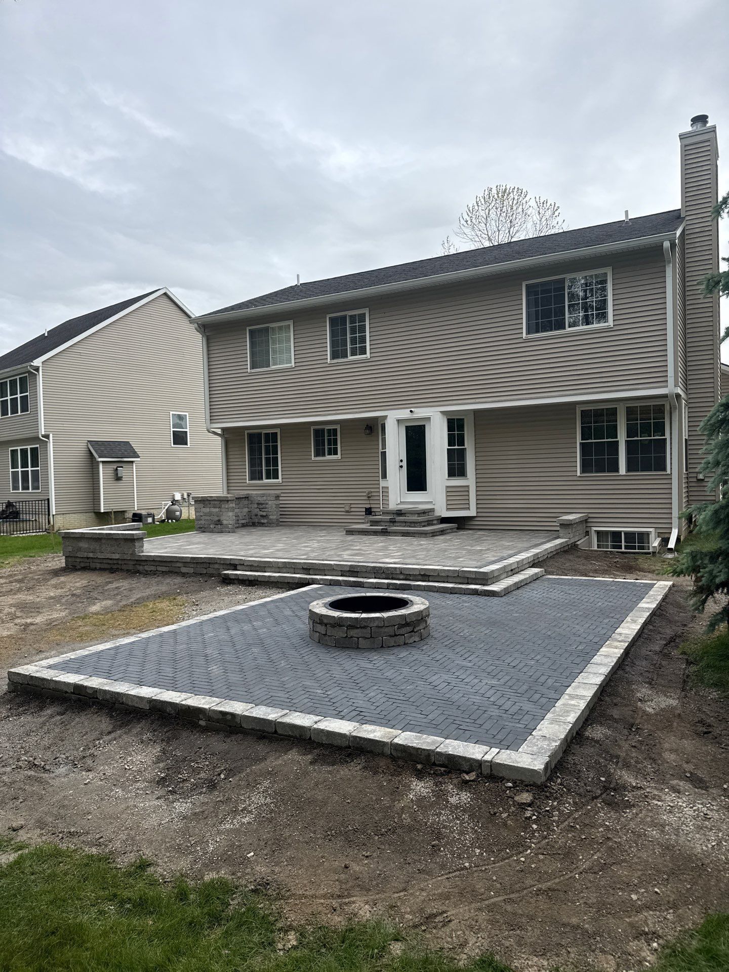 Backyard patio with gravel base, circular fire pit, and two-story house in the background