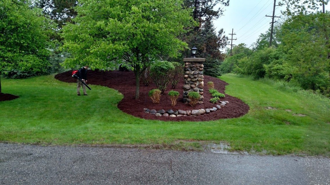 Landscaped garden bed with a stone fountain, surrounded by green lawn and trees after rain.