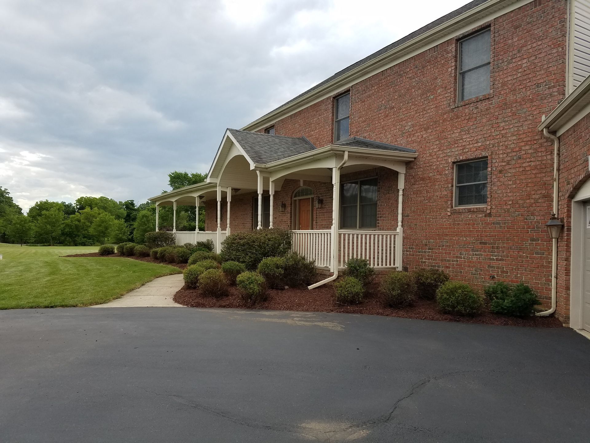 Brick apartment building with a covered porch and landscaped front entrance beside a paved driveway