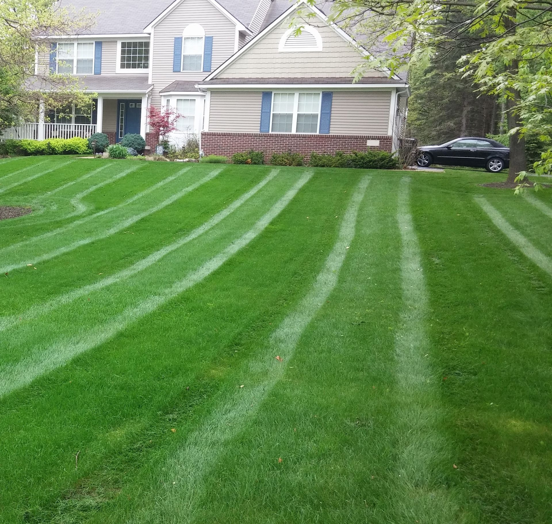 Suburban house with a freshly striped green lawn and a black car in the driveway