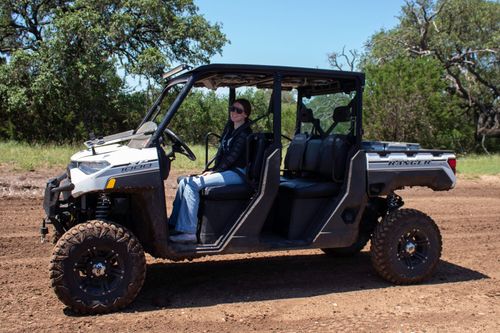 Person sitting in a white off-road utility vehicle on a dirt road with trees in the background