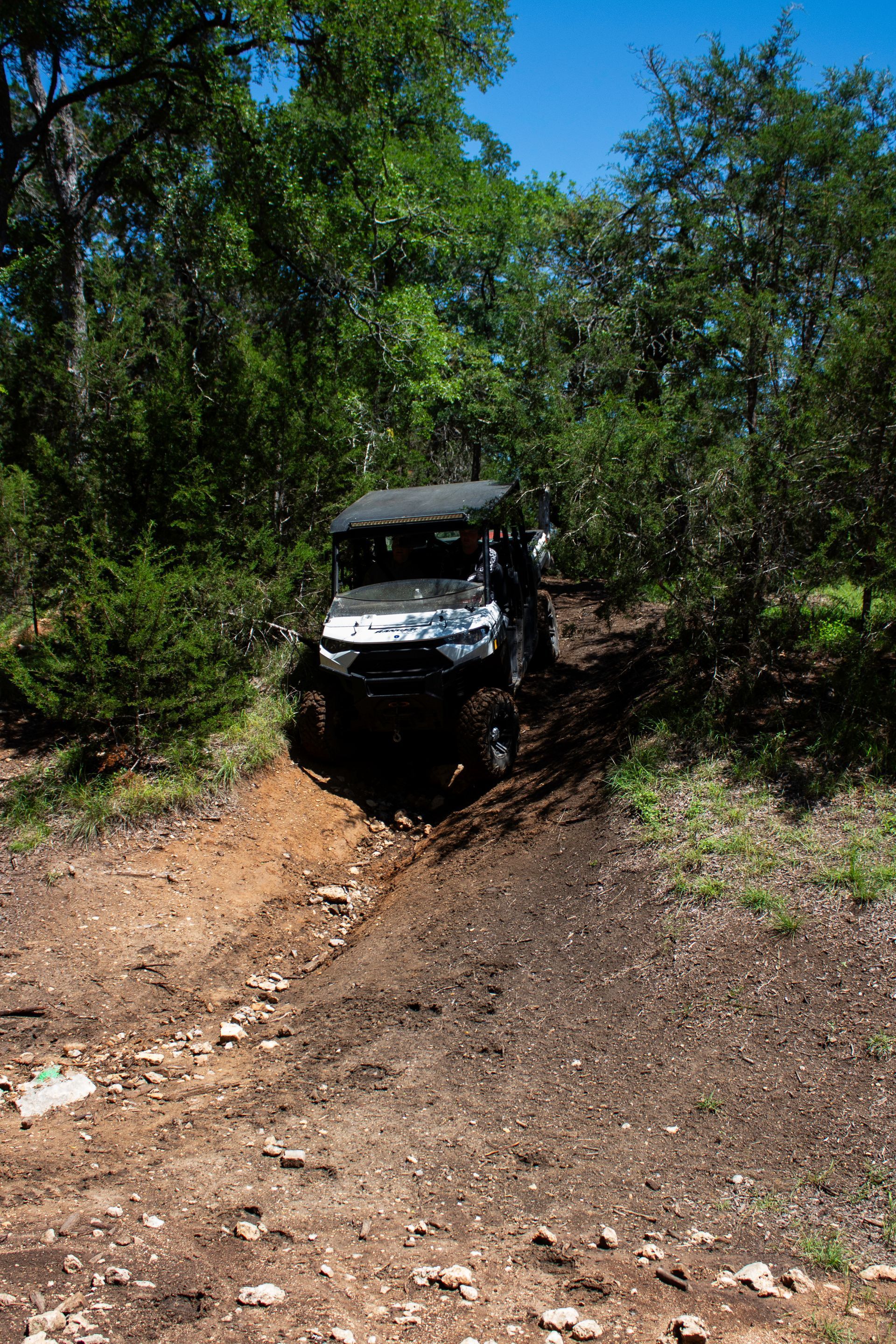 Off-road vehicle stuck in a muddy forest trail under bright sunlight