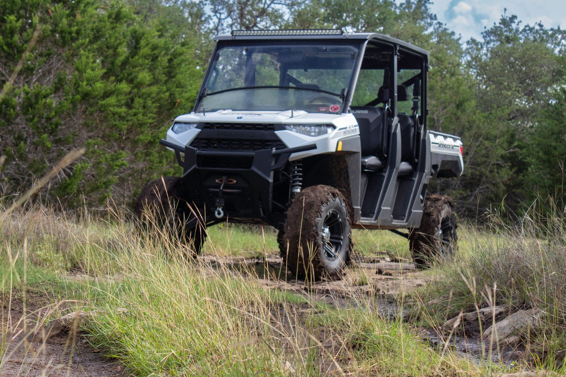 Black utility off-road vehicle driving through grassy, wooded terrain