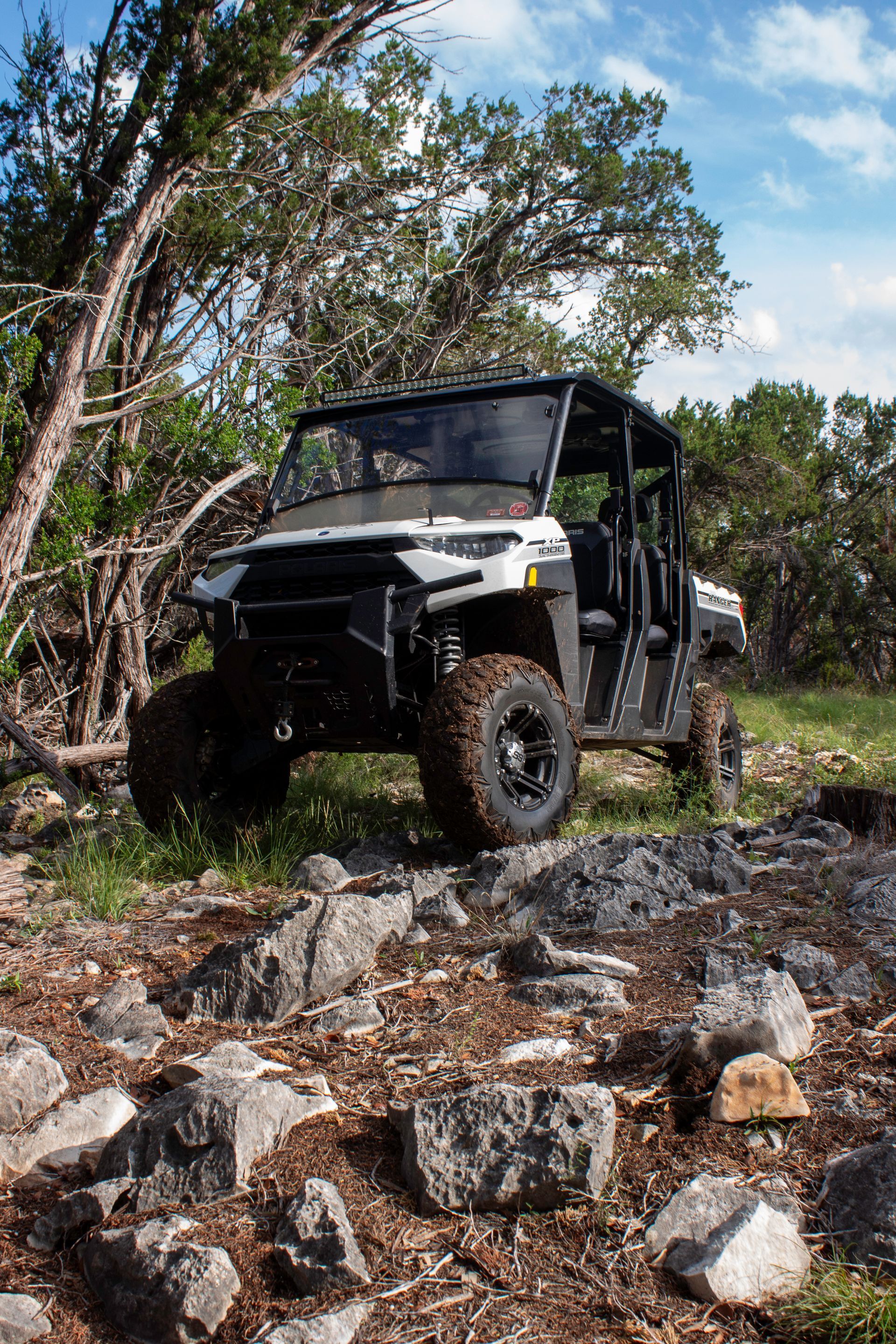 Black off-road utility vehicle navigating rocky trail in a wooded area under a blue sky