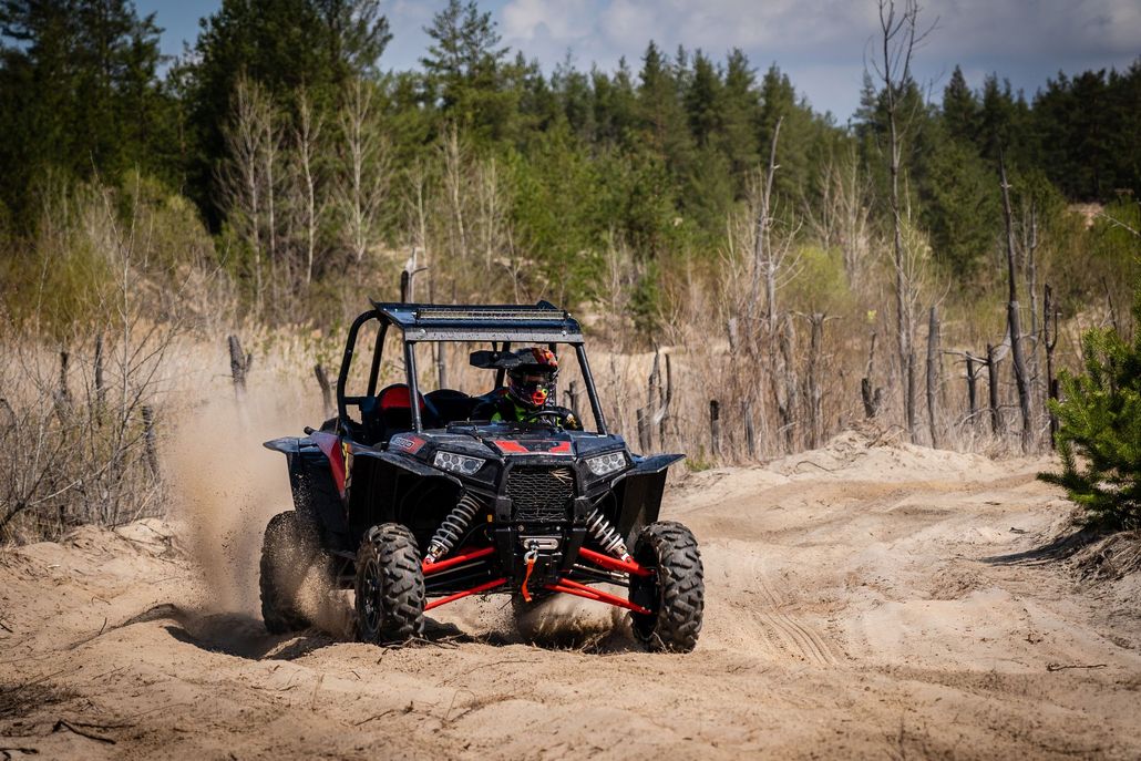 Off-road buggy kicking up dust on a sandy trail in a wooded area
